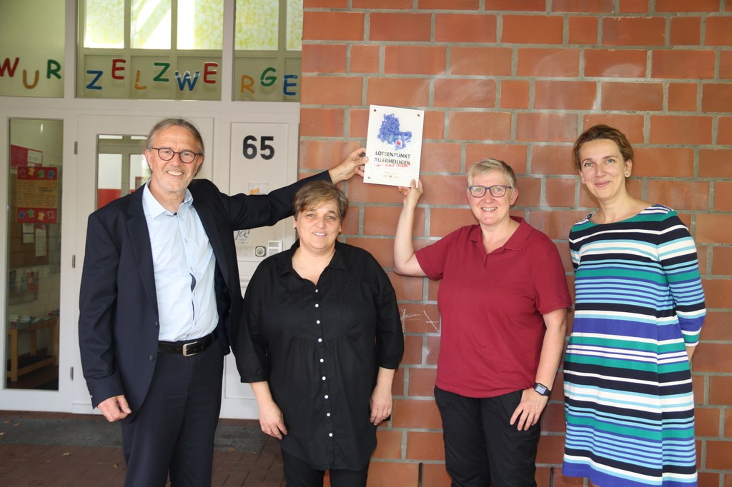 Sozialamtsleiter Michael Theven (l.) und Gudrun Jüttner, Koordinatorin der Lotsenpunkte (r.) überreicht das offizielle „Lotsenpunkt-Schild“ an Sandra Bausch, Leiterin des Familienzentrums, und Daniela Boy, Ansprechpartnerin im Lotsenpunkt Allerheiligen (v.l.).